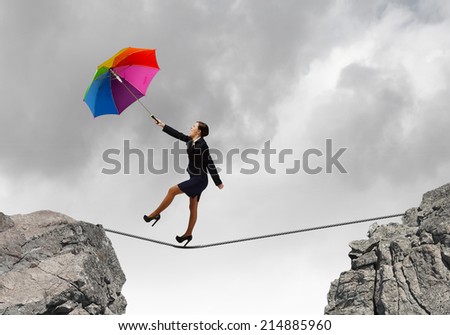 Young businesswoman walking on rope above gap with colorful umbrella