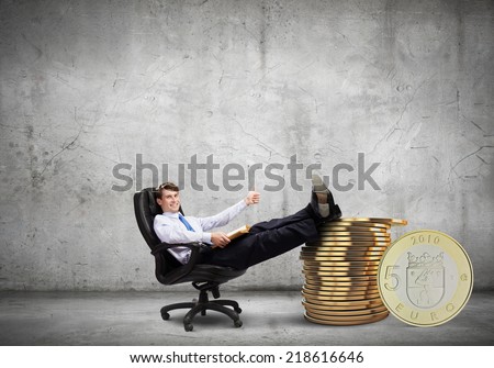 Young confident businessman sitting in chair with legs on stack of coins