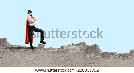 Confident man in cape and mask standing on ruins