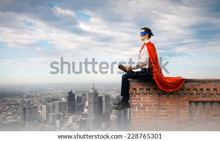 Young man in superhero costume reading book