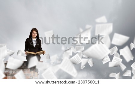 Young businesswoman sitting on building top with book in hands