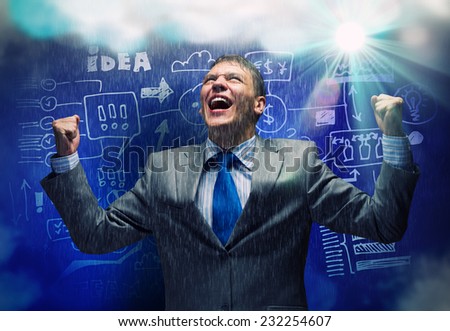 Young joyful businessman with hands up celebrating success