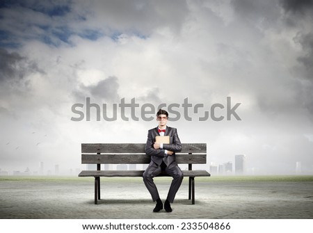 Young man in suit sitting on bench with book in hands
