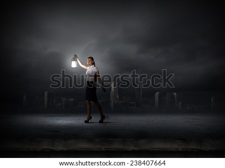 Young businesswoman walking in darkness with lantern in hand