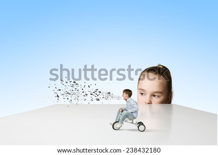 Little girl looking at boy riding three wheeled bicycle