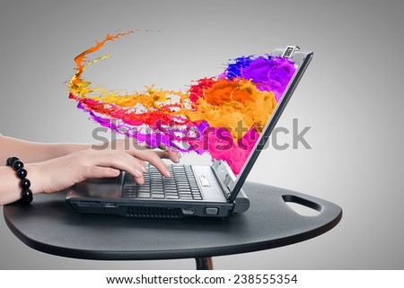 Hands of woman using laptop and colorful splashes on screen