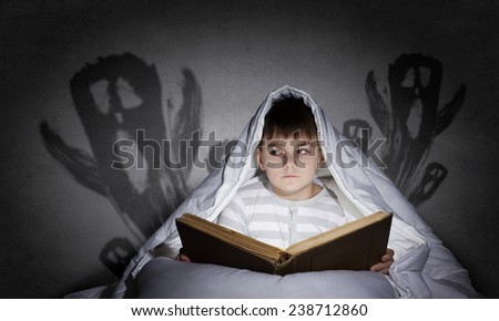 Little scared boy in bed under blanket with flashlight