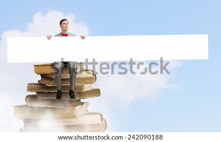 Young man with white blank banner sitting on pile of books