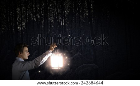 Young businessman walking with lantern in darkness