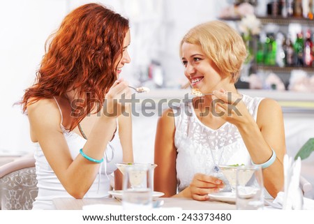 Two young pretty women sitting at cafe and eating dessert