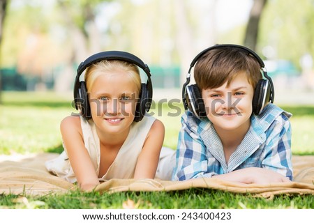 Cute boy and girl in summer park listening to music