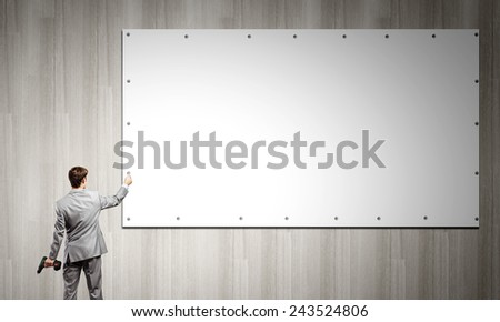 Rear view of businessman fixing blank white banner on wall