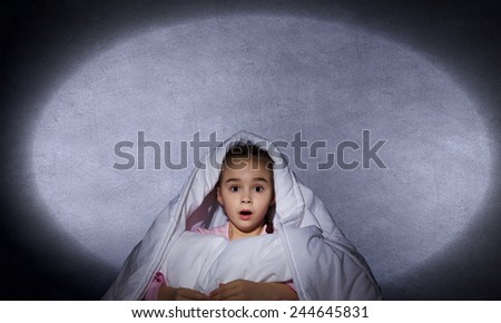 Cute scared girl sitting in bed under blanket