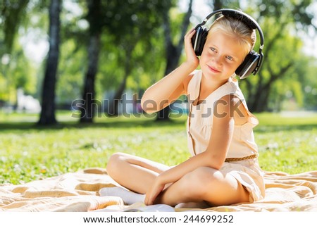 Little cute girl in summer park on blanket wearing headphones