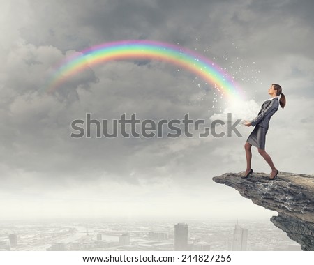 Young businesswoman on rock edge and colorful rainbow