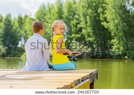 Rear view of two children sitting at bank and fishing