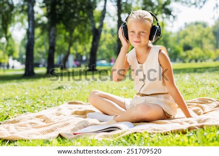 Little cute girl in summer park on blanket wearing headphones