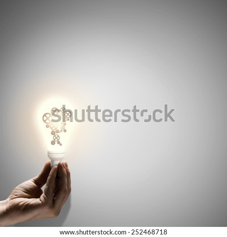 Close up of human hand holding light bulb with gears inside