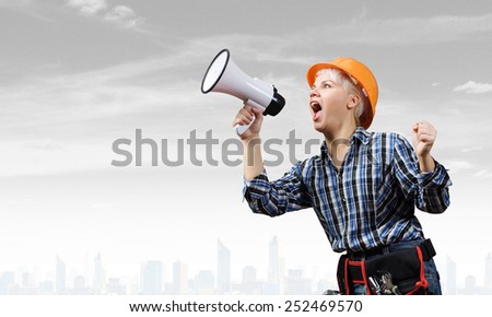 Young emotional woman builder screaming in megaphone