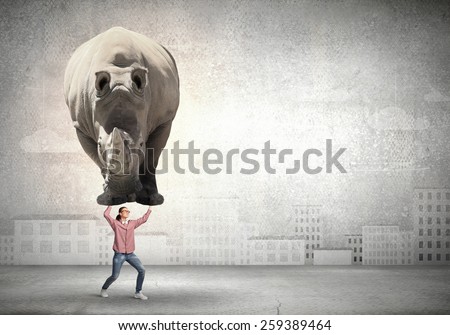 Funny young girl making effort to lift huge rhino