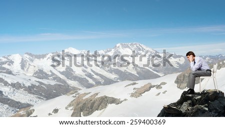 Troubled businessman sitting in chair on top of mountain