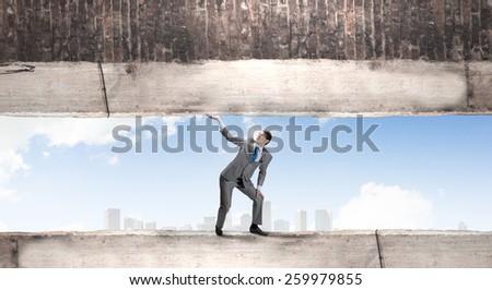 Young powerful businessman lifting brick wall above head