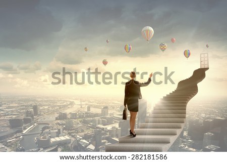 Businesswoman walking up staircase to door in sky