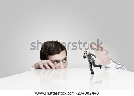 Young man looking from under table and catching running businessman