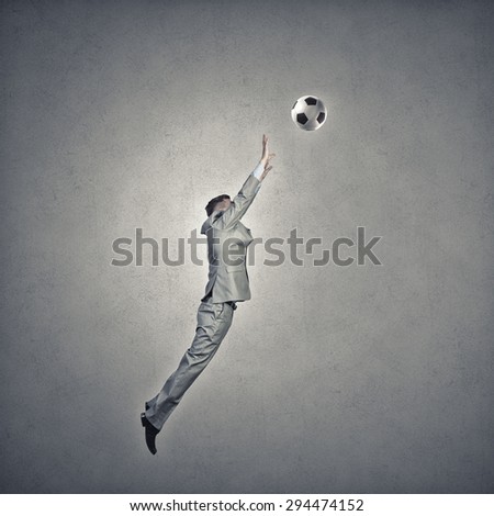 Businessman in suit jumping to hit soccer ball