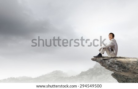 Businessman in white suit sitting on rock top