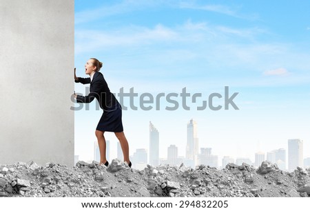 Young businesswoman making effort to move wall