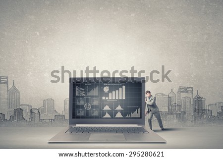 Young businessman making effort to move huge laptop