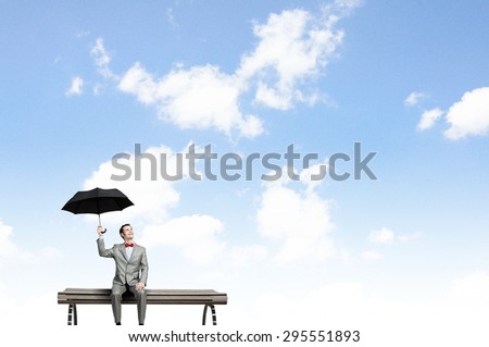 Young man in suit sitting with black umbrella in hands