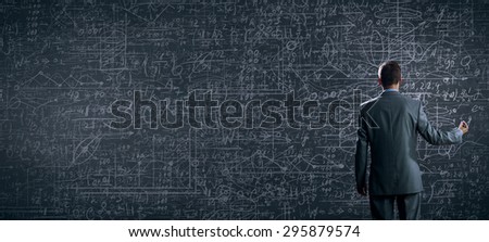 Rear view of businessman looking at chalk business sketches on wall