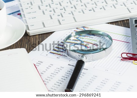 Magnifing glass and documents with analytics data lying on table