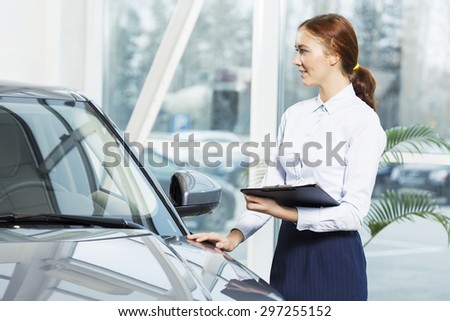 Young pretty woman dealer in showroom standing near car