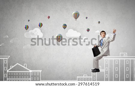 Businessman in white suit with briefcase sitting on building top
