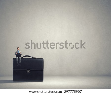 Young smiling businessman sitting on giant briefcase
