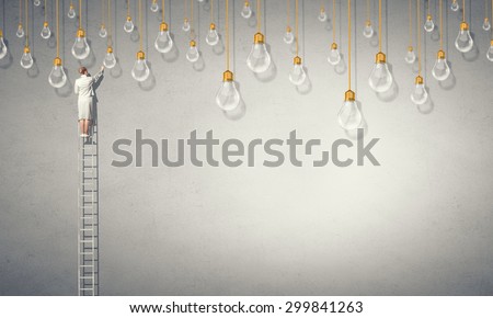 Back view of businesswoman standing on ladder and reaching light bulb
