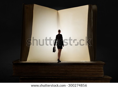 Big old opened book and miniature of businesswoman