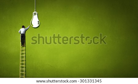 Back view of businessman standing on ladder and reaching light bulb