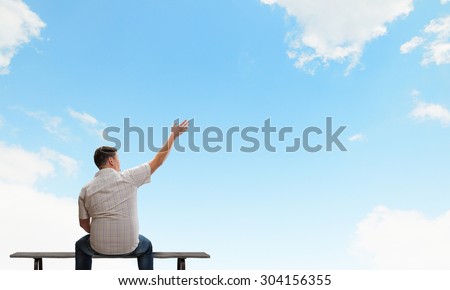Fat man sitting on bench with his back and pointing away
