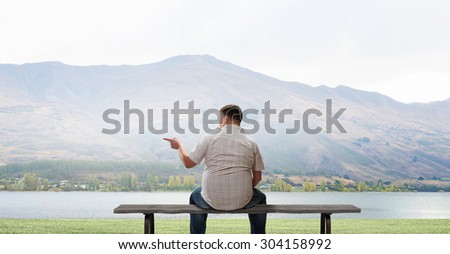 Fat man sitting on bench with his back and pointing away with finger