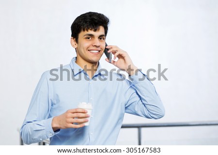 Young man with coffee in hand talking on mobile phone