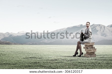 Young woman sitting on pile of books with book in hands