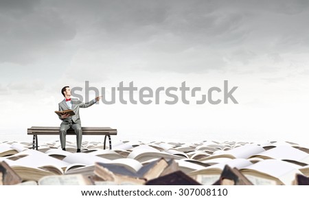 Young businessman sitting on bench with book in hands and pointing with finger