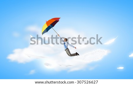 Young businessman flying high in sky on umbrella