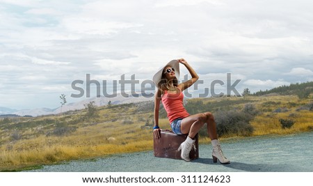 Young retro woman waiting on road with her vintage baggage