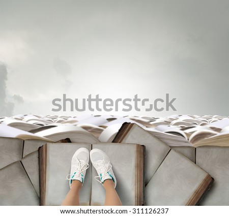 Top view of female legs in sport shoes standing on pile of books