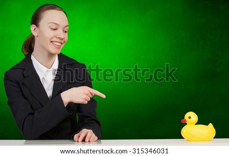 Young businesswoman pointing with finger at yellow rubber duck toy on table